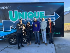 Couple and their dog with the Unique Movers team in front a moving trailer